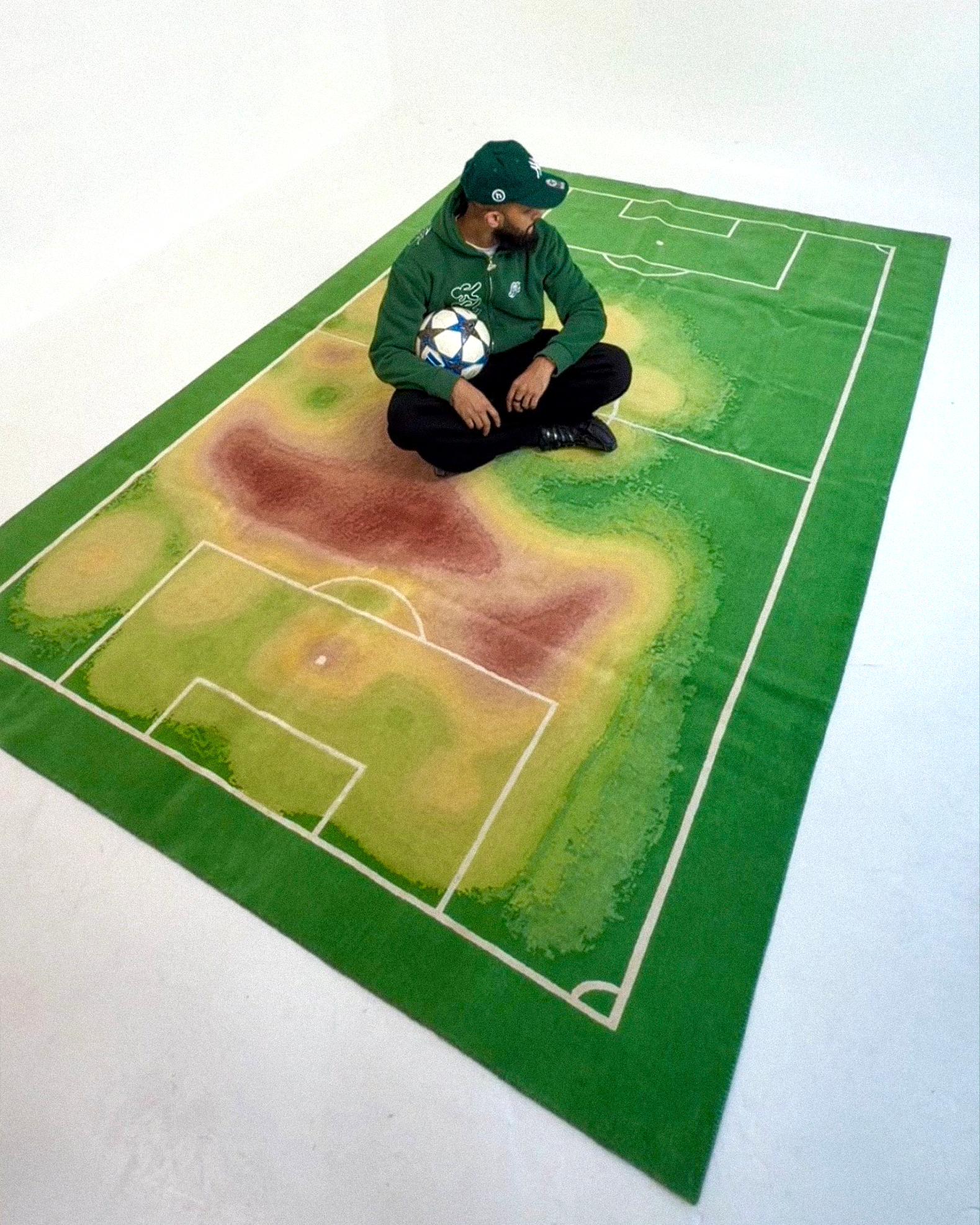 Person seated on oversized football heat map rug showing its 213 by 320 cm scale
